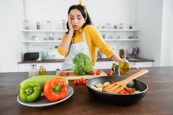 台所のテーブルの上でフライパンと野菜を背景に疲れた女の近くで — ストック写真