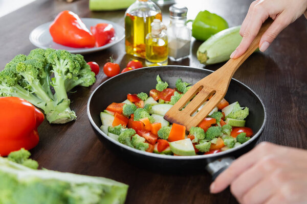 cropped view of woman mixing sliced vegetables on frying pan with spatula 