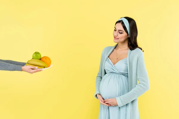 黄色い果実に閉じ込められた新鮮な果物を見ながらお腹に触れる妊婦の笑顔 — ストック写真