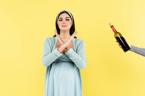 pregnant woman showing stop gesture near bottle of red wine isolated on yellow