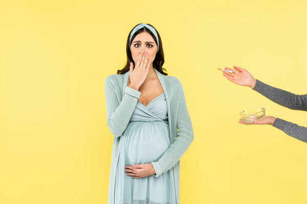 scared pregnant woman covering mouth near cigarette and ashtray isolated on yellow