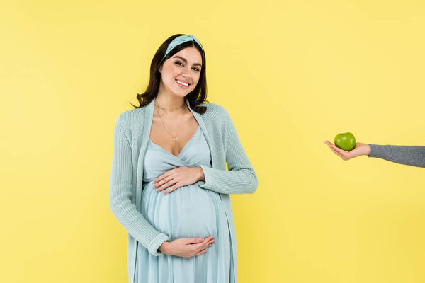 pleased woman touching belly near juicy apple isolated on yellow