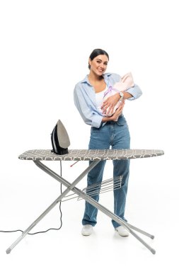 happy mother holding newborn baby near ironing board on white background clipart