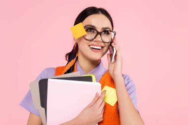 Akıllı telefonda konuşan neşeli iş kadını, pembe üzerinde izole edilmiş belgeleri tutuyor.