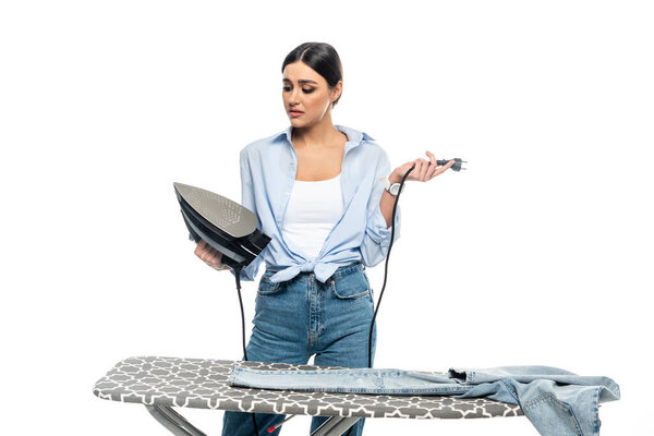 upset housewife holding broken iron near ironing board isolated on white