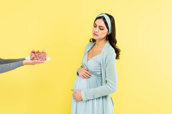 pregnant woman touching belly near tasty dessert isolated on yellow