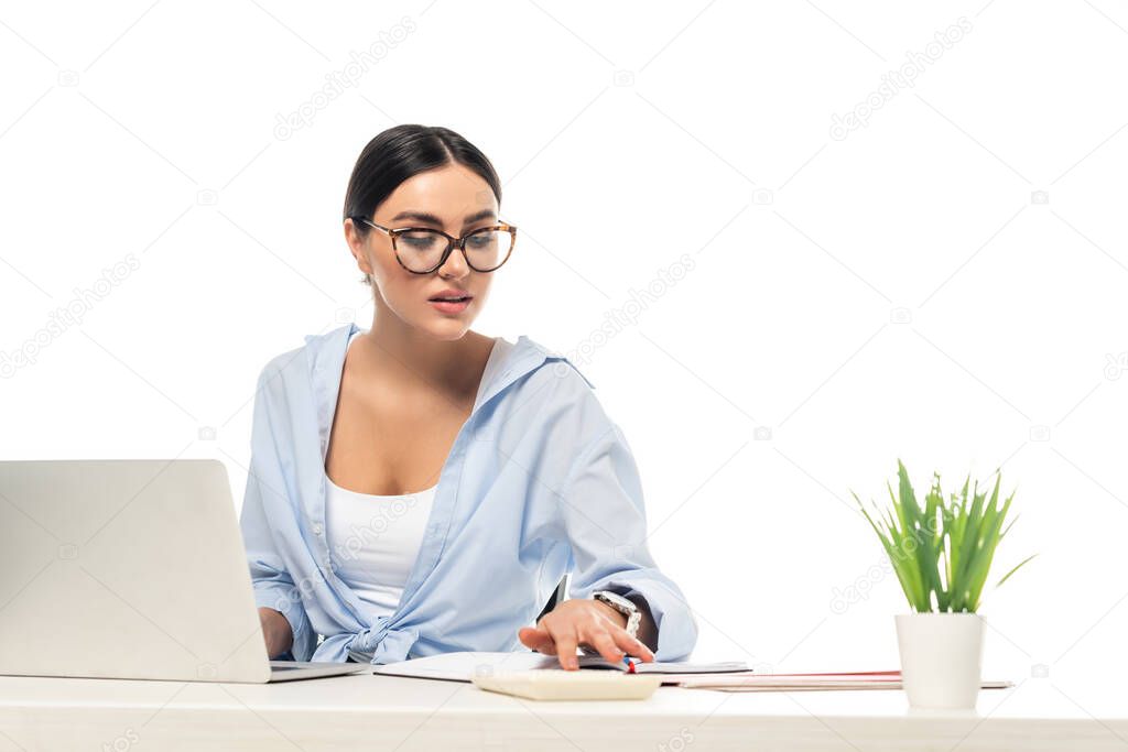 young businesswoman using calculator while working near laptop isolated on white