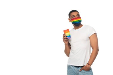 Tıbbi maskeli ve gökkuşağı renklerinde kağıt bardaklı Afro-Amerikan bir adam beyaz, lgbt kavramına izole edilmiş.