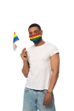 Küçük Igbt bayrağı ve gökkuşağı renginde tıbbi maskeli Afro-Amerikan bir adam beyaza izole edilmiş kameraya bakıyor.