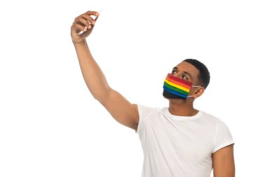 Afrikalı Amerikalı bir adam lgbt renginde tıbbi maske takıyor ve beyazlar içinde selfie çekiyor.