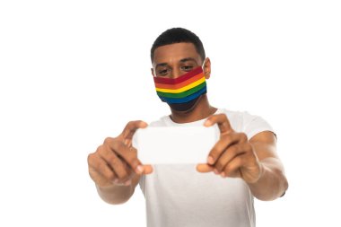 Afrika kökenli Amerikalı adam güvenlik maskesi takıyor ve beyaz telefondan izole edilmiş bir şekilde selfie çekiyor.