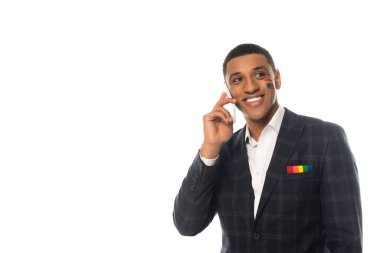 Yüzüne Igbt bayrağı çizilmiş neşeli Afro-Amerikan işadamı beyaz bir cep telefonuyla konuşuyor.