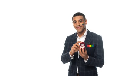 Yüzünde lgbt bayrağı olan gülümseyen Afrikalı Amerikalı adam elinde alyansla beyaza boyanmış.