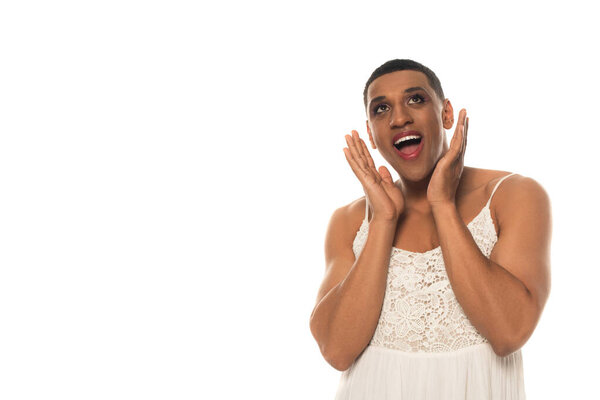 amazed african american gay man in sundress holding hands near face isolated on white