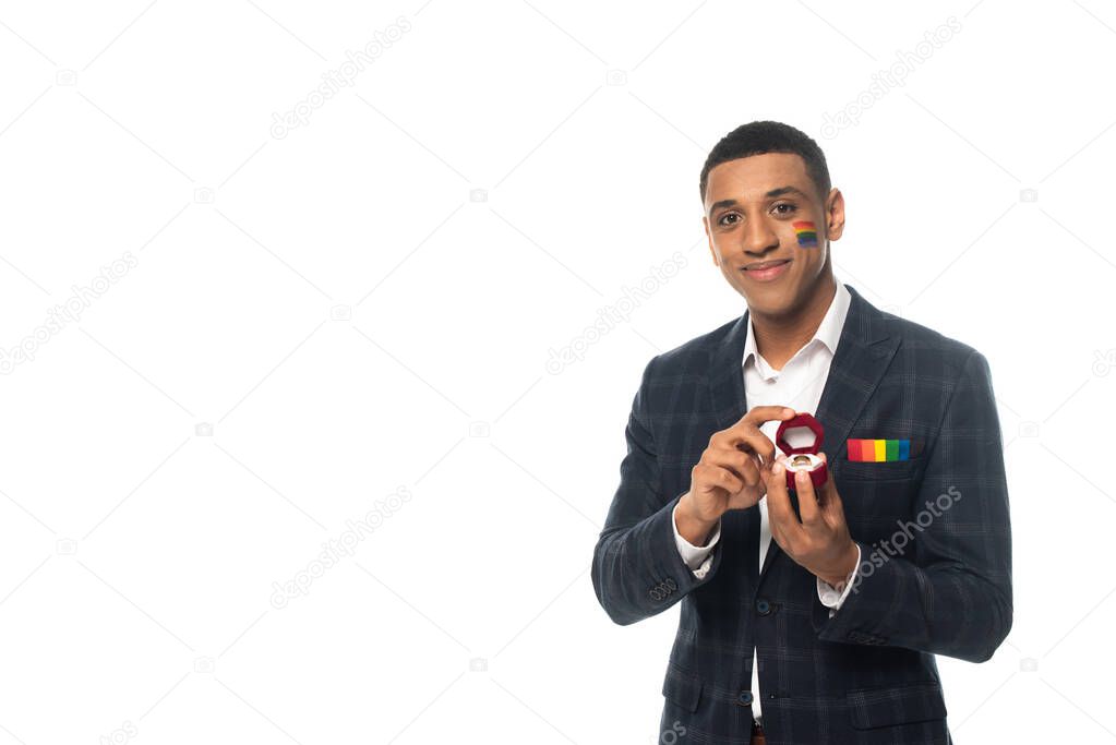 smiling african american man with lgbt flag painted on face holding wedding ring isolated on white