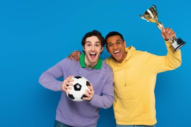 heyecan verici ırklar arası futbol oyuncuları top ve kupayı mavi renkte tutuyorlar.