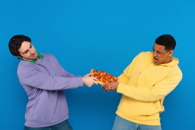 interracial friends emotionally sharing one pizza slice isolated on blue clipart