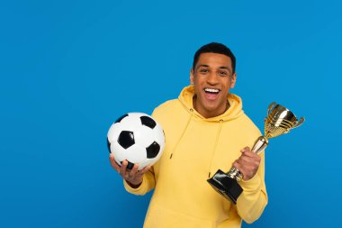 Gülümseyen Afro-Amerikan genç adam futbol ve kupa ile mavi üzerine izole