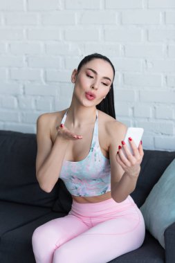Spor giyinen esmer kadın cep telefonuyla video görüşmesi sırasında hava öpücüğü veriyor.