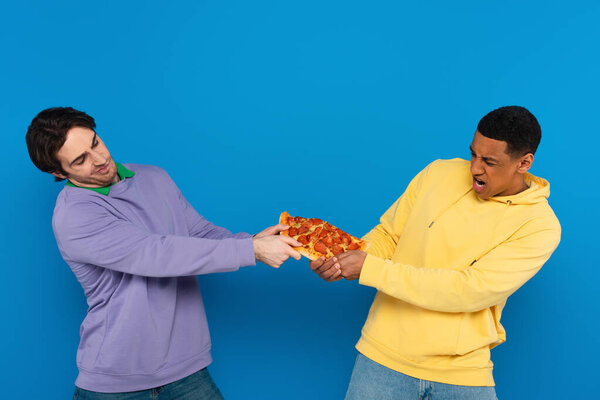 interracial friends emotionally sharing one pizza slice isolated on blue