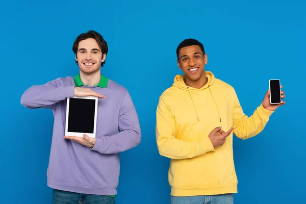 Szczęśliwy Międzyrasowy Przyjaciele Pokazując Urządzenia Cyfrowe Pusty Ekran Odizolowany Niebieski — Zdjęcie stockowe