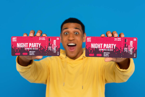 улыбающийся африканский американец показывает билеты на концерт в руках, изолированных на голубом