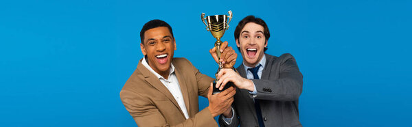 interracial friends in suits celebrating success with prize cup in hands isolated on blue, banner 