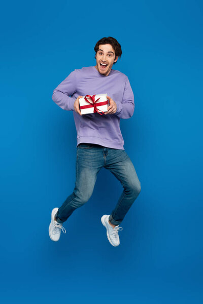 возбужденный молодой человек левитации с подарочной коробке на голубом фоне
