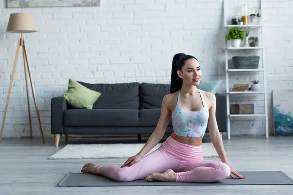 Smilende Kvinde Kigger Væk Mens Sidder Yogamåtten Derhjemme - Stock-foto