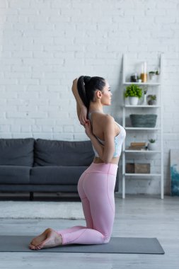 Diz çöküp yoga yapan sportif kadın elleri arkada.