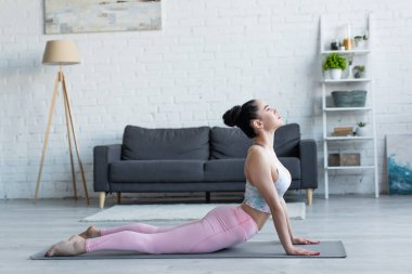 Yüksek kobra pozuyla yoga yapan esmer bir kadının yan görüntüsü.