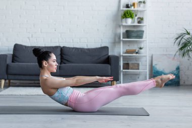 Esmer kadının yoga minderinde poz verirken yan görünümü.