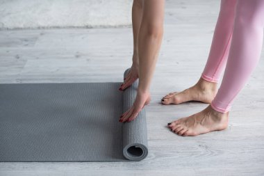 Çıplak ayaklı bir kadının evde yoga minderini açması.