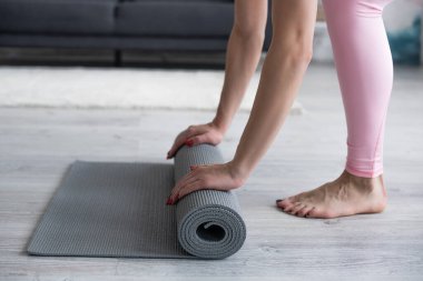 Çıplak ayaklı bir kadının yoga minderini açarken kısmi görüntüsü