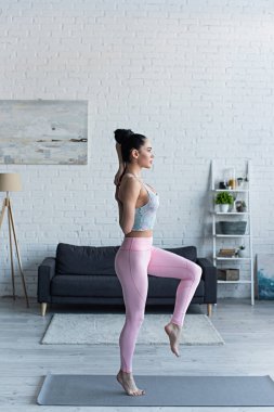 Evde yoga yaparken elleri arkada duran genç bir kadının yan görüntüsü.
