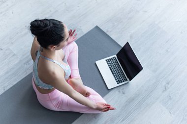 Nilüfer çiçeğiyle meditasyon yapan bir kadının laptopun yanındaki yoga minderinde poz verişi. 