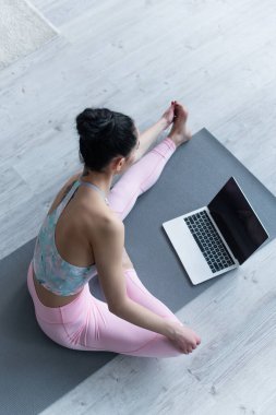 Laptop 'un yanında yoga yapan esmer kadının boş ekranlı görüntüsü.