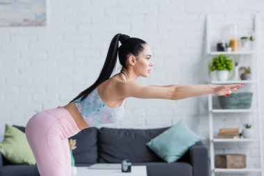 Spor giysili esmer bir kadının yan görünüşü. Uzamış elleriyle öne eğilme egzersizi yapıyor.