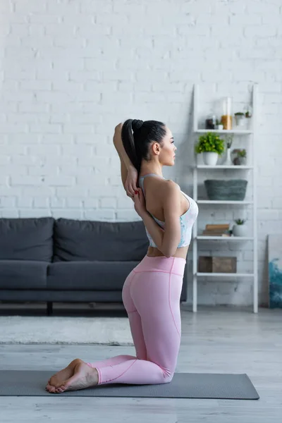 sportive woman practicing yoga in kneeling pose with hands behind back
