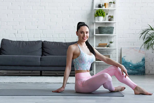 Spor Kıyafetli Mutlu Bir Kadın Yoga Minderinde Otururken Kameraya Gülümsüyor — Stok fotoğraf