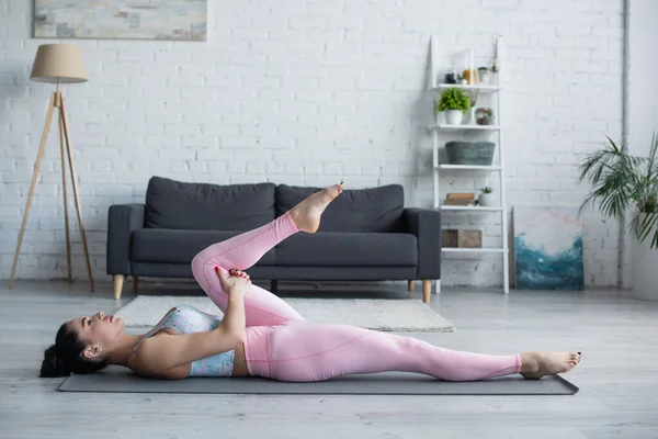 女子穿着运动服躺在瑜伽垫上脱风姿势的侧视图 — 图库照片