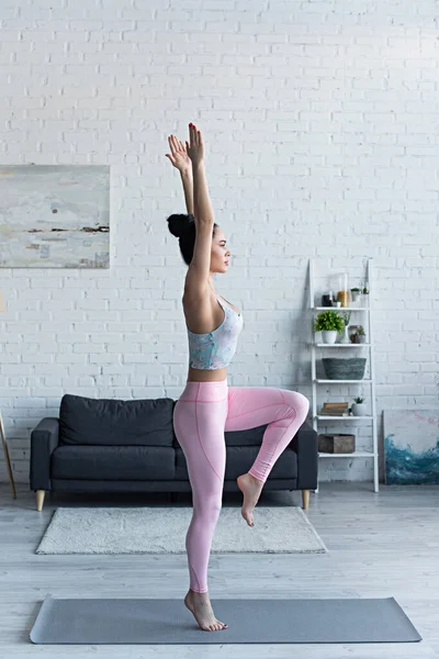 黑发女子高举双手单腿站在一边练瑜伽的侧视图 — 图库照片