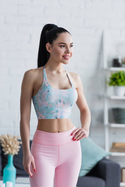 young woman in sportswear smiling while standing with hand on hip