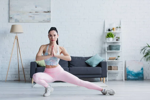 sportive woman looking at camera while training in gate pose at home
