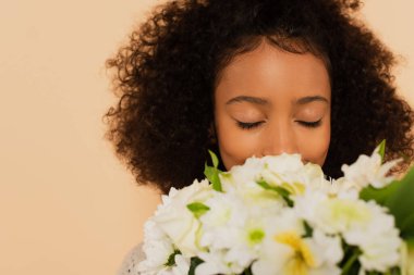 african american preteen girl smelling bouquet of daisies with closed eyes isolated on beige clipart