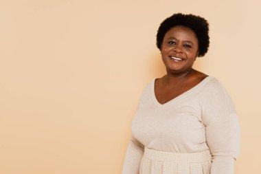 Pastel giysili orta yaşlı neşeli Afro-Amerikan kadın bej üzerine izole edilmiş