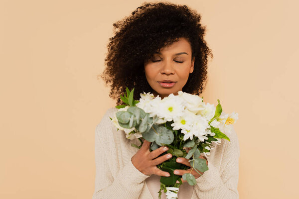 african american woman smelling bouquet of daisies with closed eyes isolated on beige