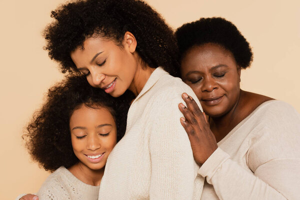 african american grandmother embracing with daughter and granddaughter with closed eyes isolated on beige