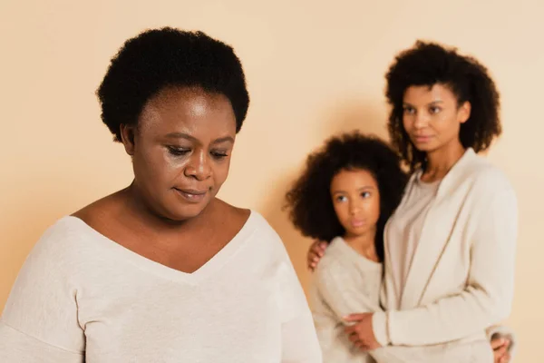 African American Mother Embracing Daughter Looking Sad Grandmother Beige Background — Stock Photo, Image