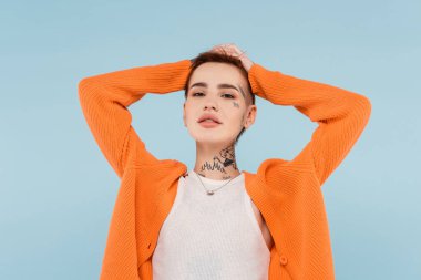 Dövmeleri olan modaya uyan genç bir kadın. Mavi üzerinde kızıl saç ayarlıyor.